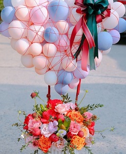 Pink and blue balloons 25 in number on the sticks of a basket filled with orange and red flowers
