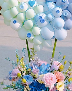 25 Blue Balloons cluster on top held with sticks on a basket of pink blue and yellow roses flowers
