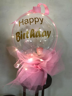 Happy birthday print on the transparent balloon white net wrapping and gold bow in a box with string light