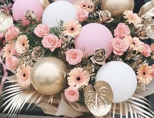 6 Pink Gold and White balloons placed in between gold leaves and 20 pink roses and gerberas